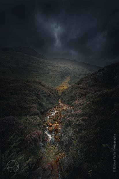 A steep glen seen from above, a stream threading down through it under heavy cloud