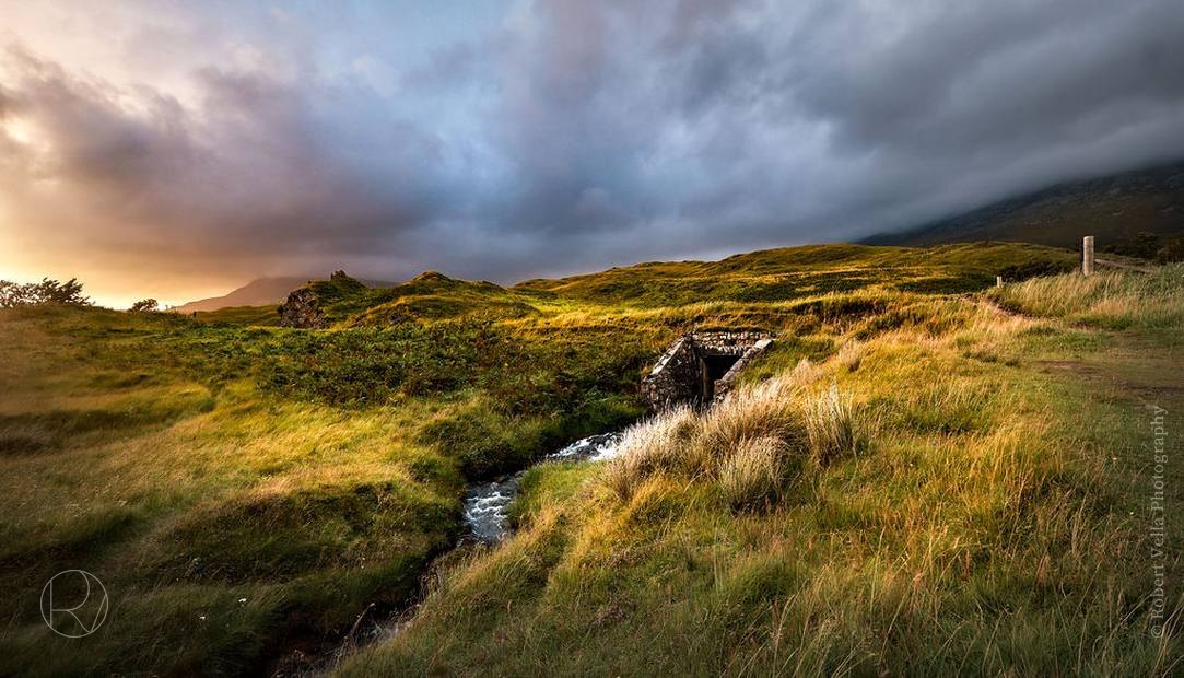 A small stream running through moorland grass, the sky breaking open at dusk