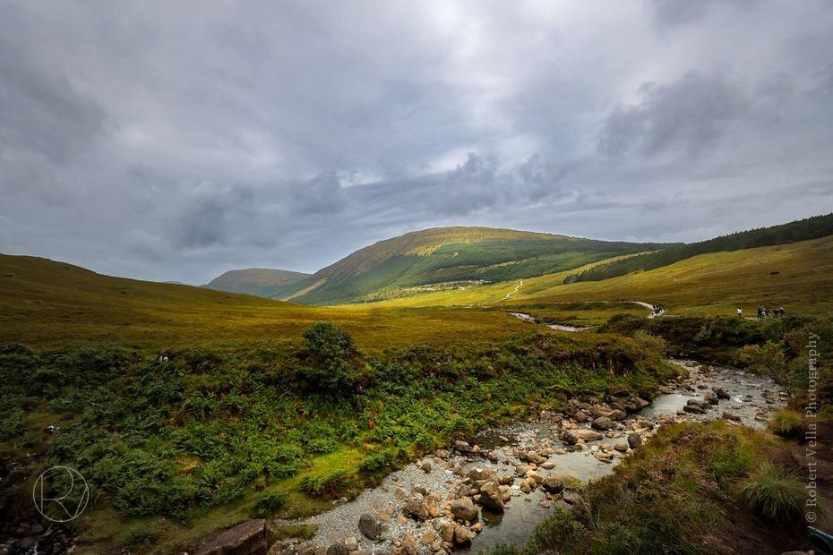 Green hills with a river winding along the valley floor under a grey sky