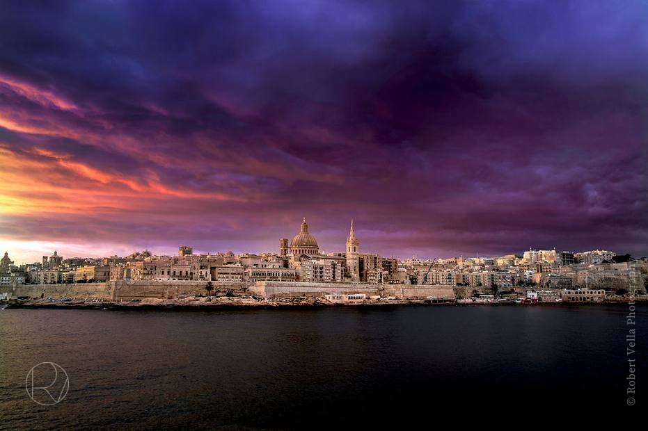 Valletta seen across the water at dusk, the skyline lit under a purple and orange sky