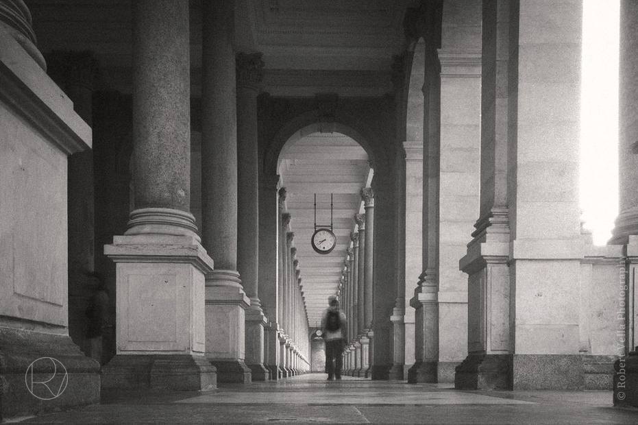 A long colonnade in black and white, one figure walking through it