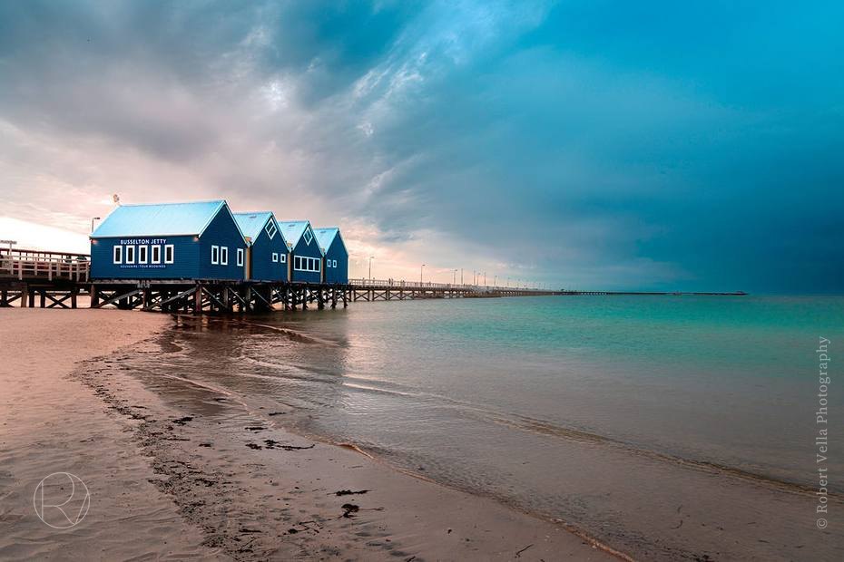 A row of blue bathing huts on a wooden jetty over turquoise water